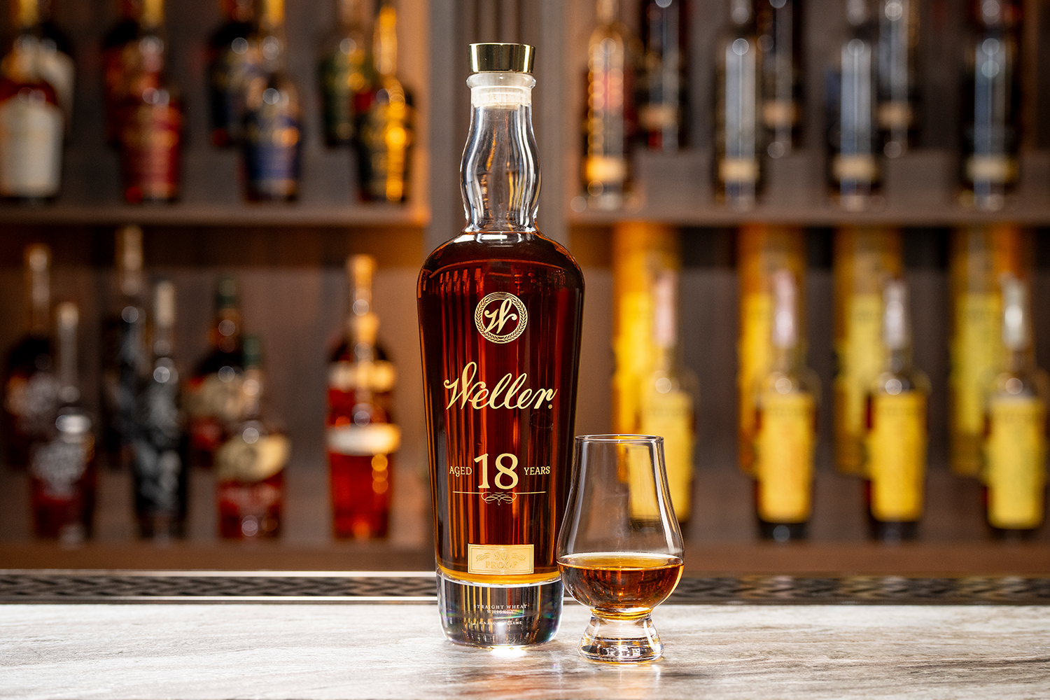 A bottle of Weller 18 Year Old sitting on a bar next to a small glass of the whiskey