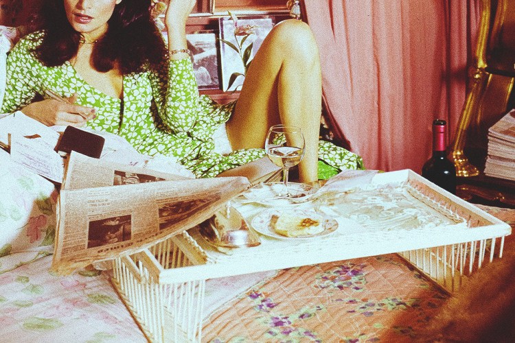 A woman in bed with a tray that includes a glass of wine