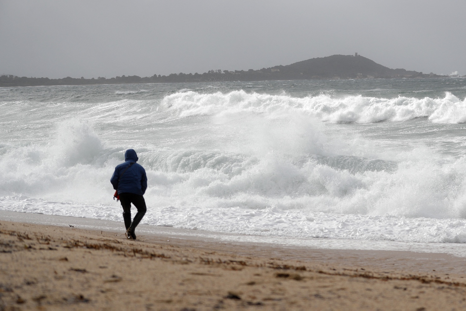 A man walks on a beach in winter, watching the waves.