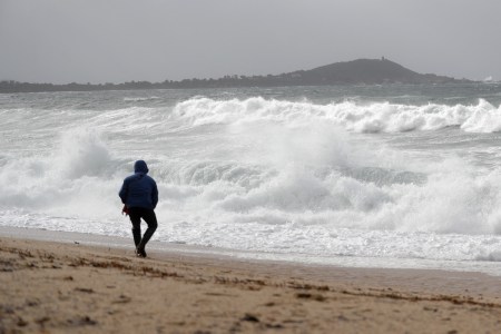 A man walks on a beach in winter, watching the waves.