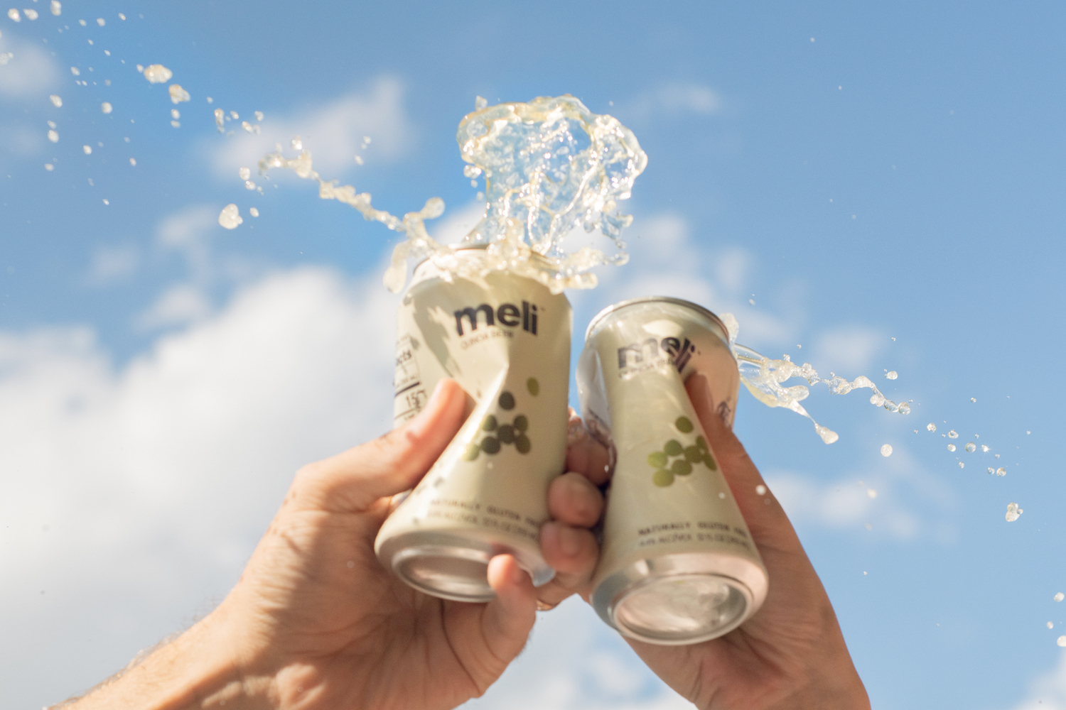 two people cryshing cans of meli beer in front of a blue sky