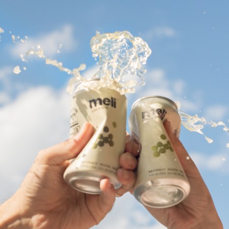 two people cryshing cans of meli beer in front of a blue sky