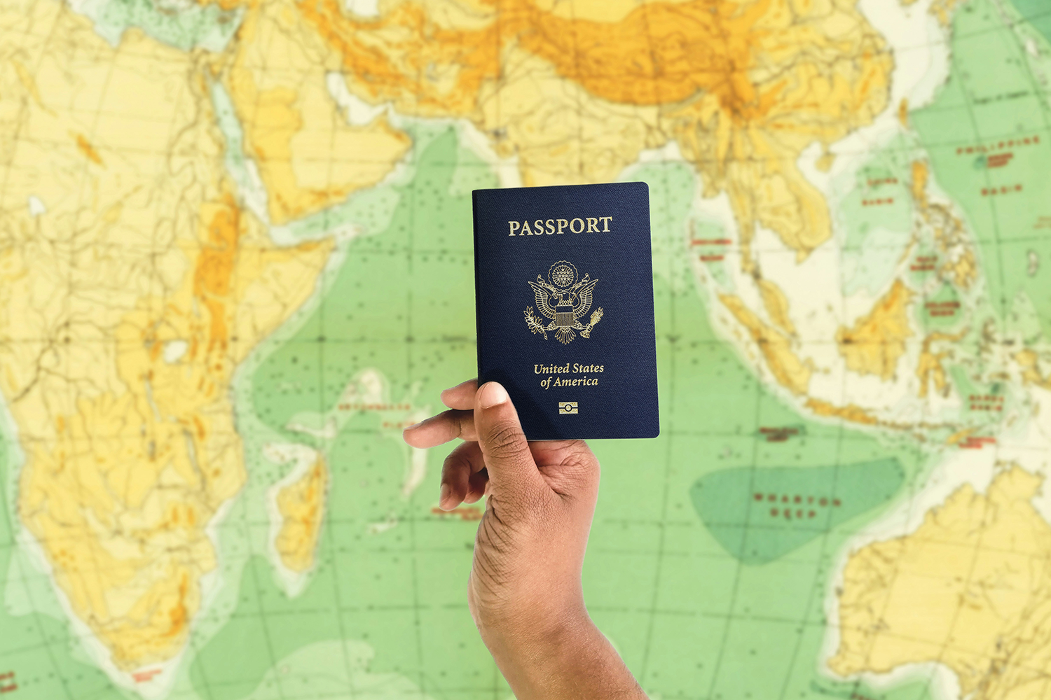 someone holding up a u.s. passport in front of a green and yellow map