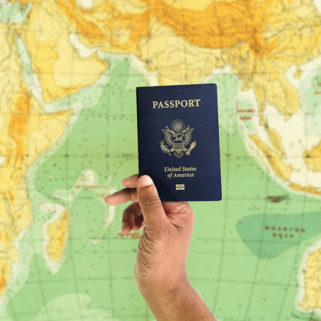 someone holding up a u.s. passport in front of a green and yellow map