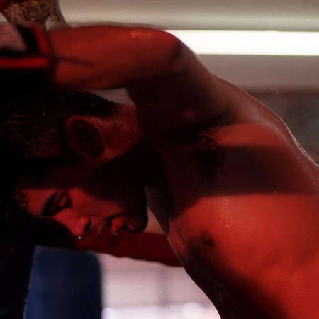 A boxer leans against the wall, shirtless and sweaty.