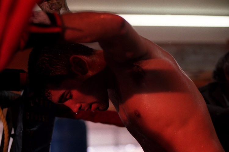 A boxer leans against the wall, shirtless and sweaty.