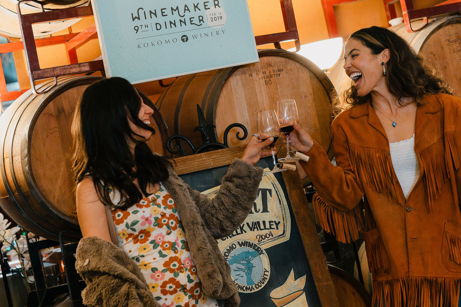 two young women toasting with goblets of red wine in front of wooden barrels