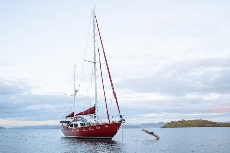 A man dives from a red sail boat.
