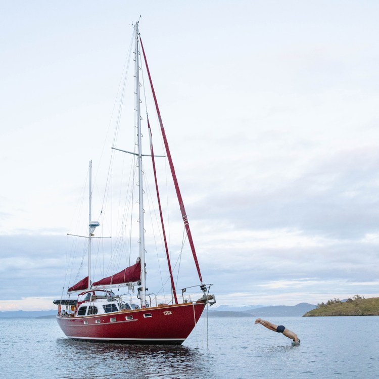 A man dives from a red sail boat.