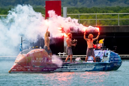 The three Maclean brothers Jamie, Ewan and Lachlan in an ocean rowboat, lighting celebratory flares.