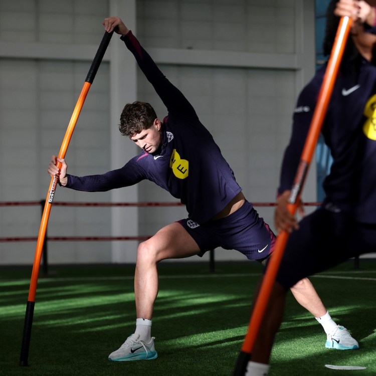 Some soccer players stretching with a weighted stick.
