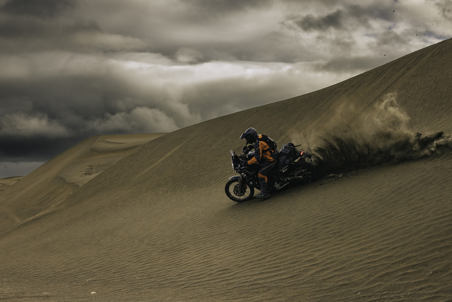 A man on a motorcycle going down a sand hill.