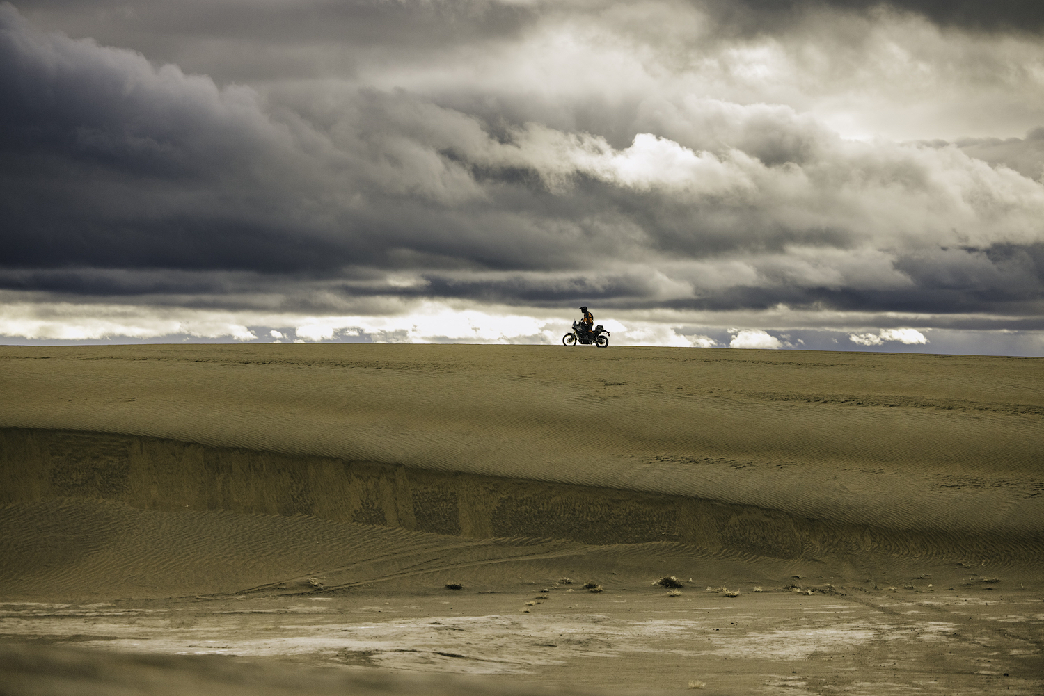 A man on a motorcycle in sand.