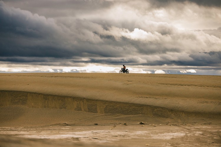 A man on a motorcycle in sand.