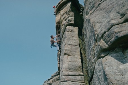 Chris Hamper ascends a rock wall, with a perfectly blue sky behind him.