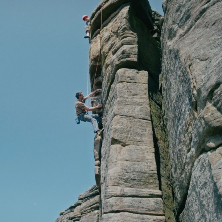 Chris Hamper ascends a rock wall, with a perfectly blue sky behind him.