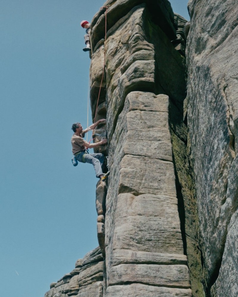 Chris Hamper ascends a rock wall, with a perfectly blue sky behind him.
