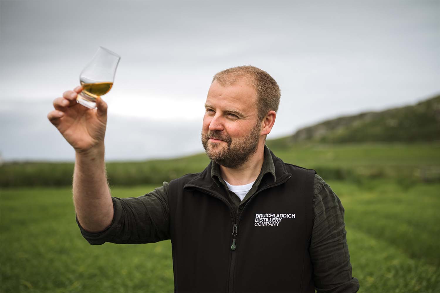 Bruichladdich Adam Hannett inspecting a glass of The Laddie Rye in a rye field at Coull Farm Islay