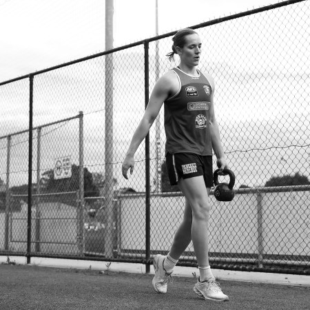 A woman carrying a kettlebell in the style of a suitcase carry.