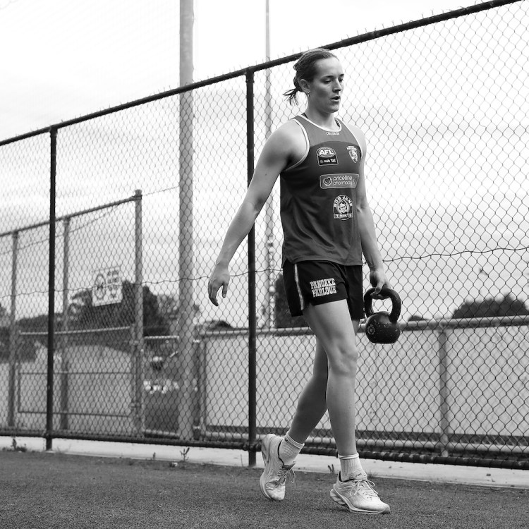 A woman carrying a kettlebell in the style of a suitcase carry.