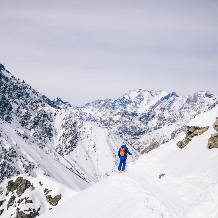 A skier on a narrow path with the Andes mountains in the background at Portillo, the legendary ski resort in Chile