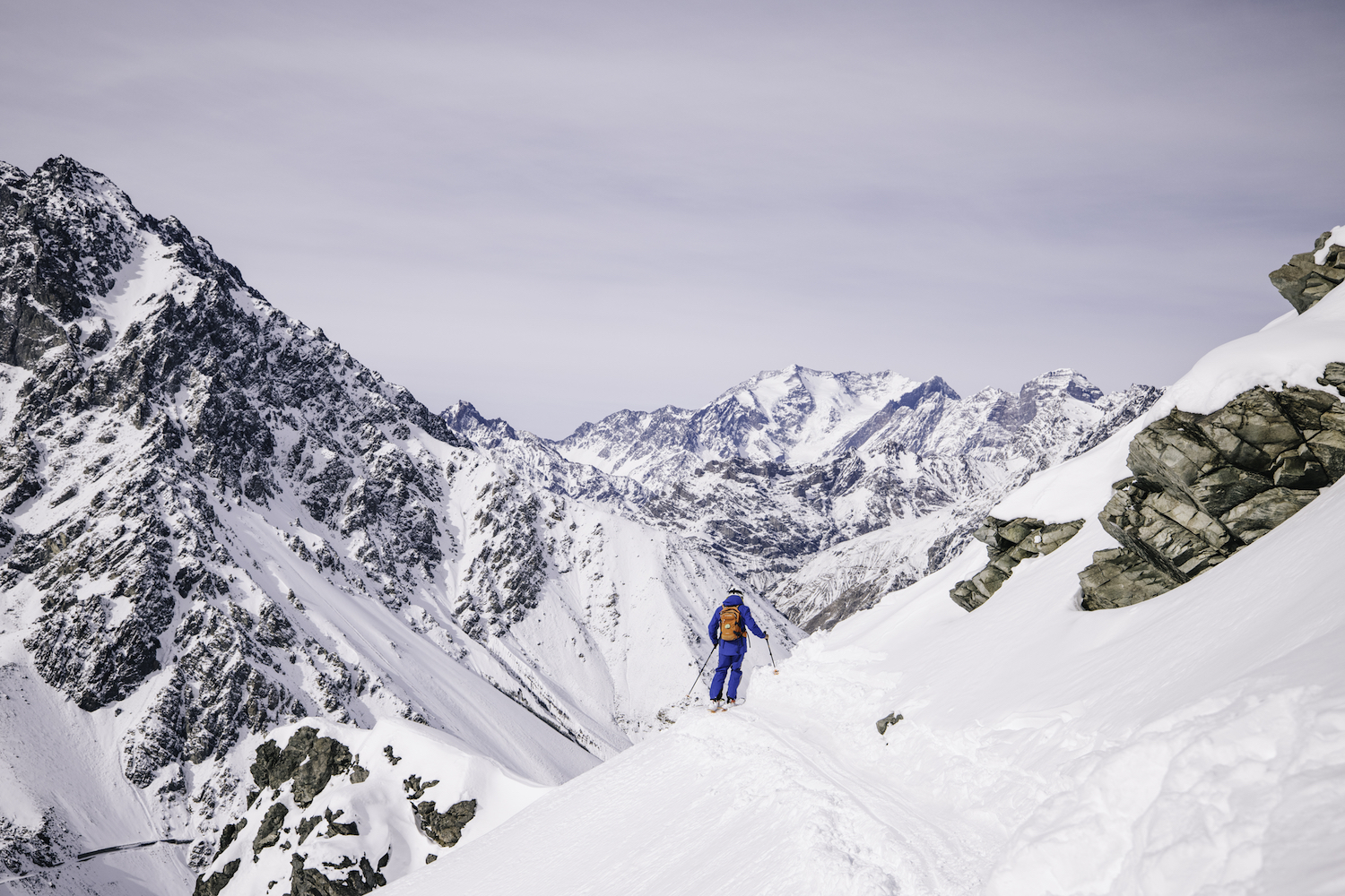 A skier on a narrow path with mountains in the background.