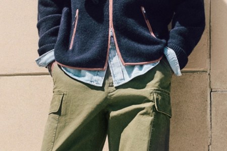 A person wearing a navy blue fleece jacket with orange trim, a light blue denim shirt, and olive green cargo pants.