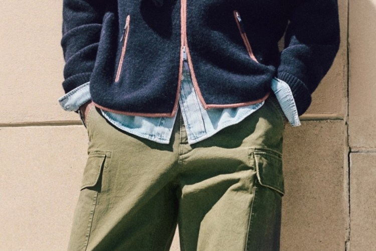 A person wearing a navy blue fleece jacket with orange trim, a light blue denim shirt, and olive green cargo pants.