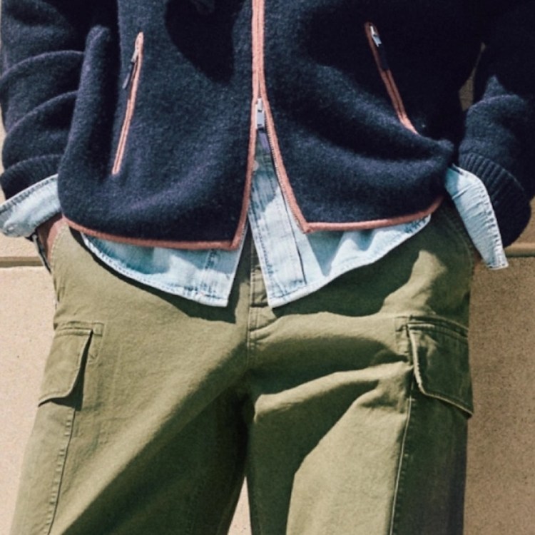 A person wearing a navy blue fleece jacket with orange trim, a light blue denim shirt, and olive green cargo pants.
