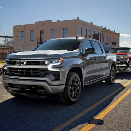 A Chevrolet Silverado truck towing a classic car on a trailer