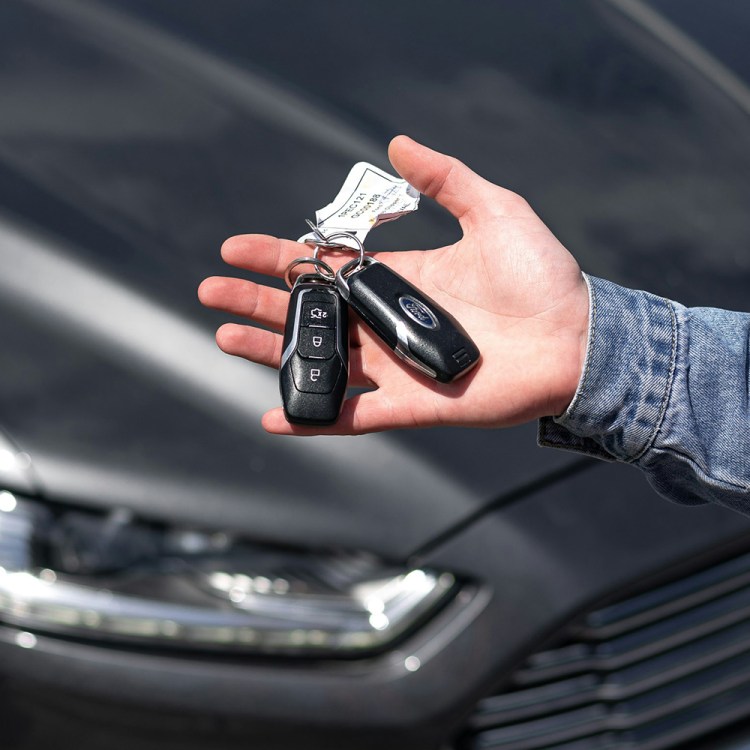 A man holding keys to a new car made by Ford with the vehicle in the background