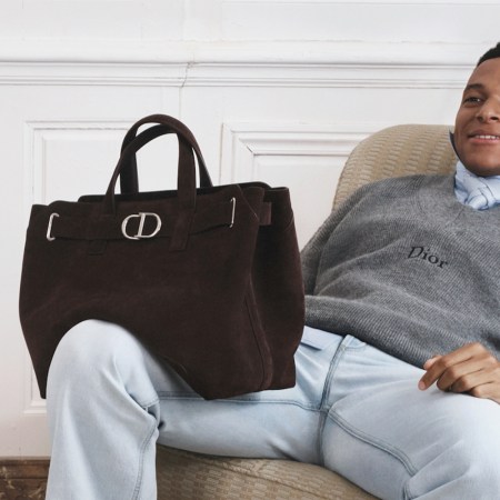 Soccer player Kylian Mbappé sitting on a chair with a brown suede Dior bag