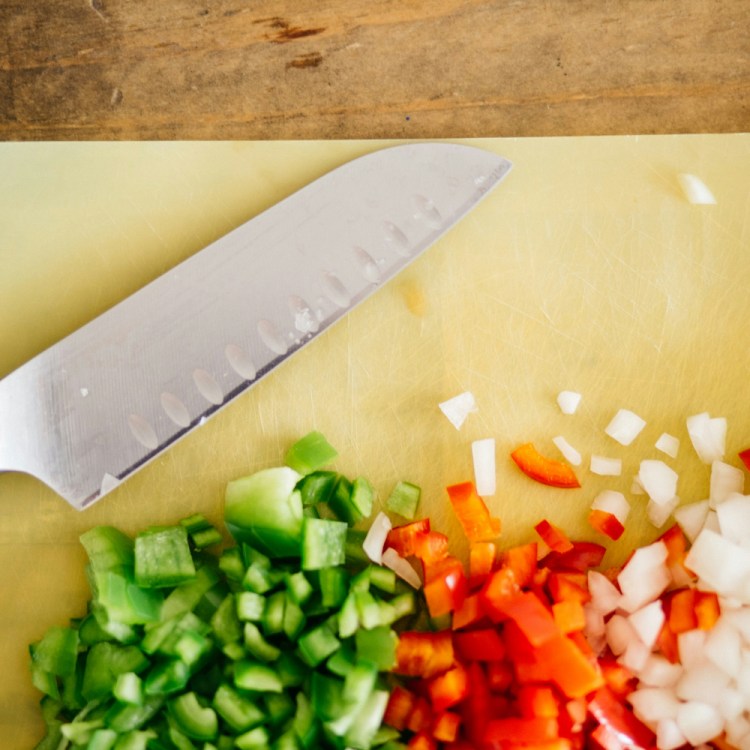 A knife next to chopped vegetables.