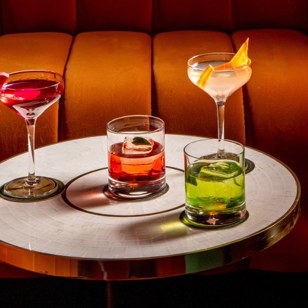 A small table topped with four cocktails, including Gin & Tonics and Martinis, in front of an orange banquette