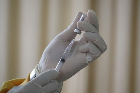 A gloved hand with a syringe getting a vaccine shot ready