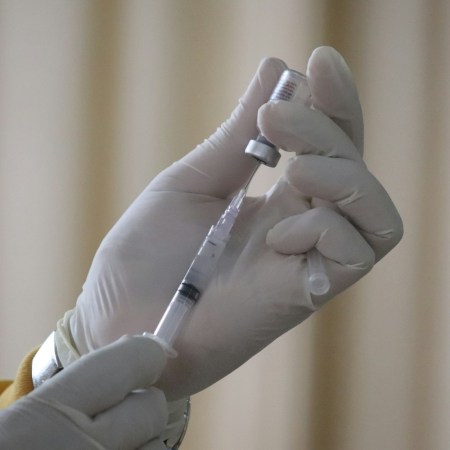 A gloved hand with a syringe getting a vaccine shot ready
