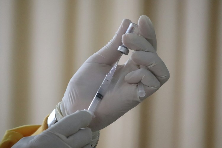A gloved hand with a syringe getting a vaccine shot ready