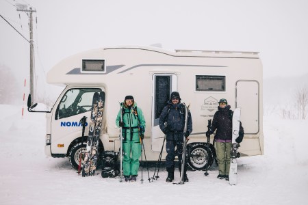 A trio of skiers stand in front of an RV.