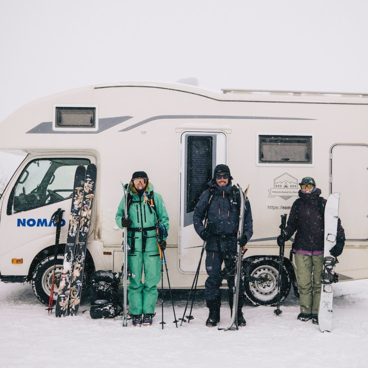 A trio of skiers stand in front of an RV.