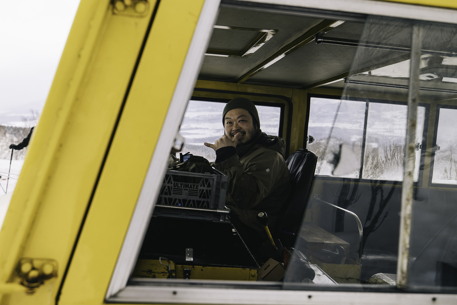 A Japanese man in a snowcat giving the camera a "shaka" gesture.