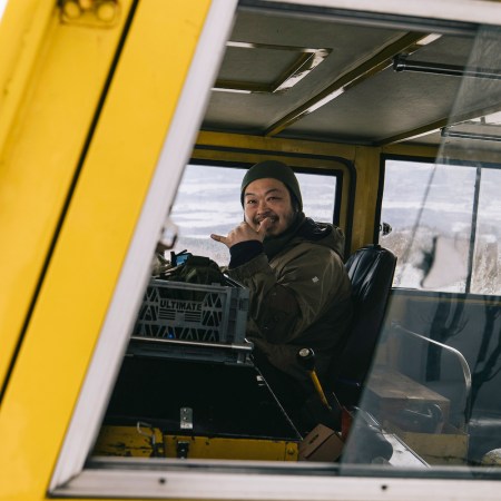 A Japanese man in a snowcat giving the camera a "shaka" gesture.