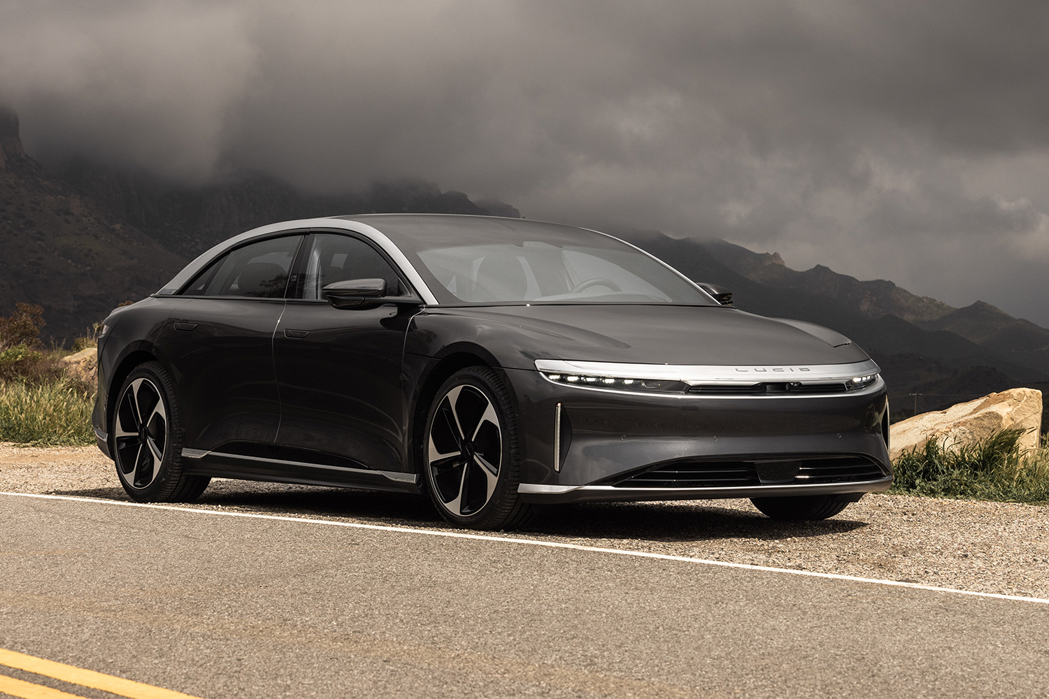 The Lucid Air Touring sitting on the side of a road with mountains and gray clouds in the background