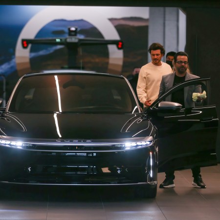 Orlando Bloom in a white sweatshirt picking up a luxury EV called the Lucid Air