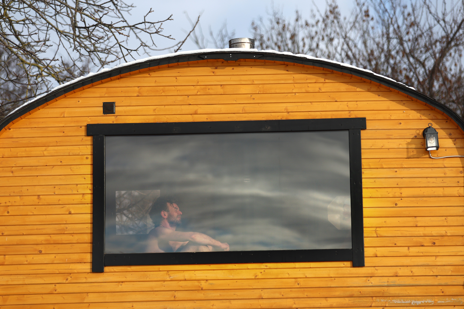 A man sitting in a wooden sauna, seen through the window.