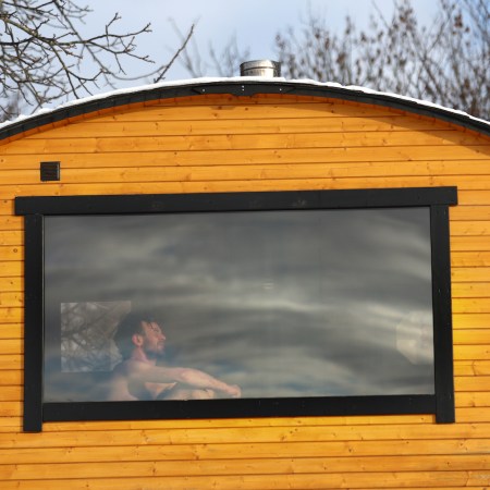 A man sitting in a wooden sauna, seen through the window.