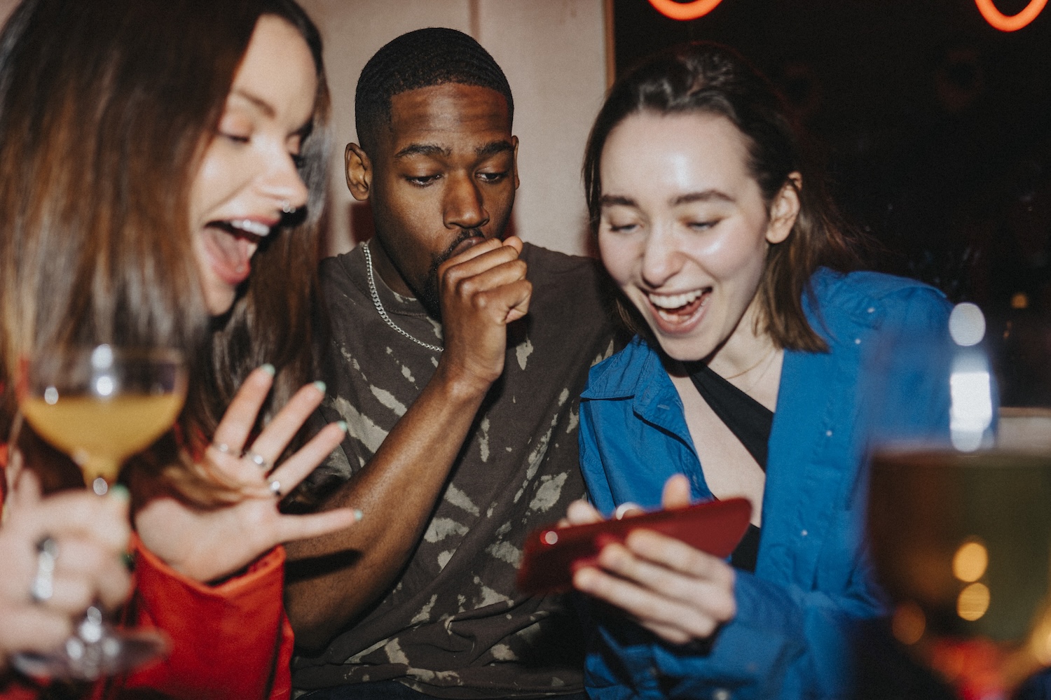 Happy woman sharing smart phone with male and female friends at nightclub