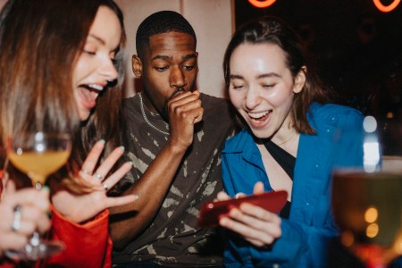 Happy woman sharing smart phone with male and female friends at nightclub