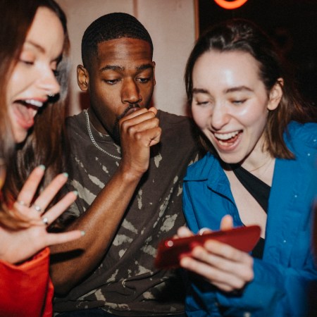 Happy woman sharing smart phone with male and female friends at nightclub
