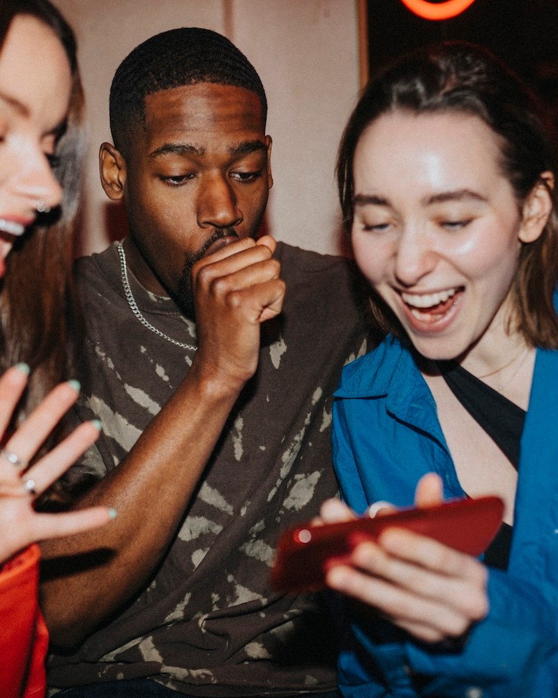 Happy woman sharing smart phone with male and female friends at nightclub