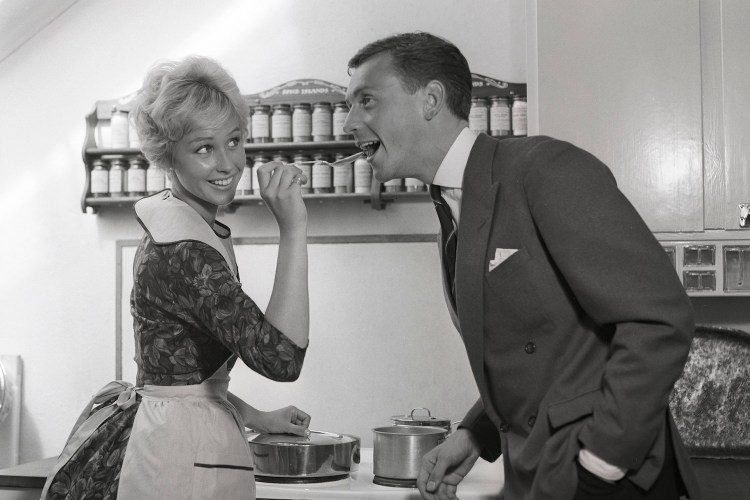 In the kitchen 1950s. A young couple in their kitchen. She is making him taste the food and puts a spoon in his mouth. Sweden 1959 Kristoffersson ref CG35 (Photo by Sjöberg Bildbyrå/ullstein bild via Getty Images)